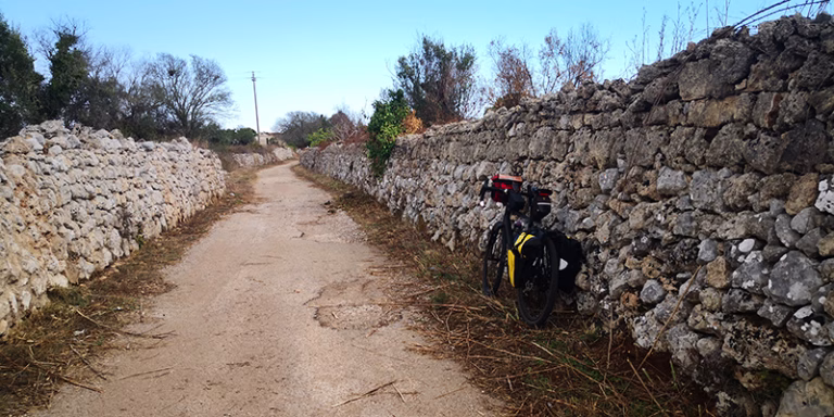 stradina asfaltata tra muri a secco alti bicicletta patu 1 768x384